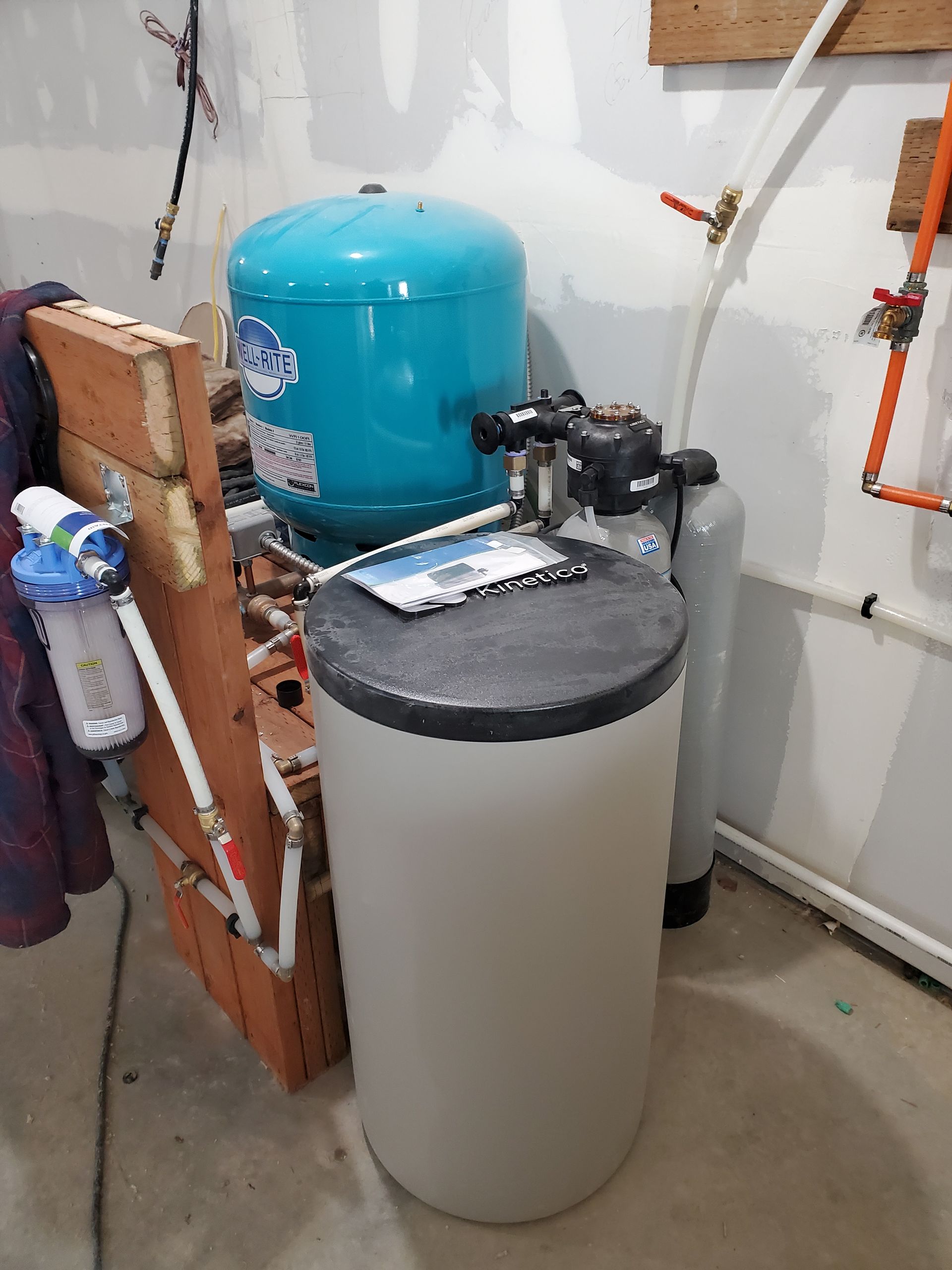 Water filtration and softening system in a basement.  Blue pressure tank, cylindrical tanks, and connected plumbing.