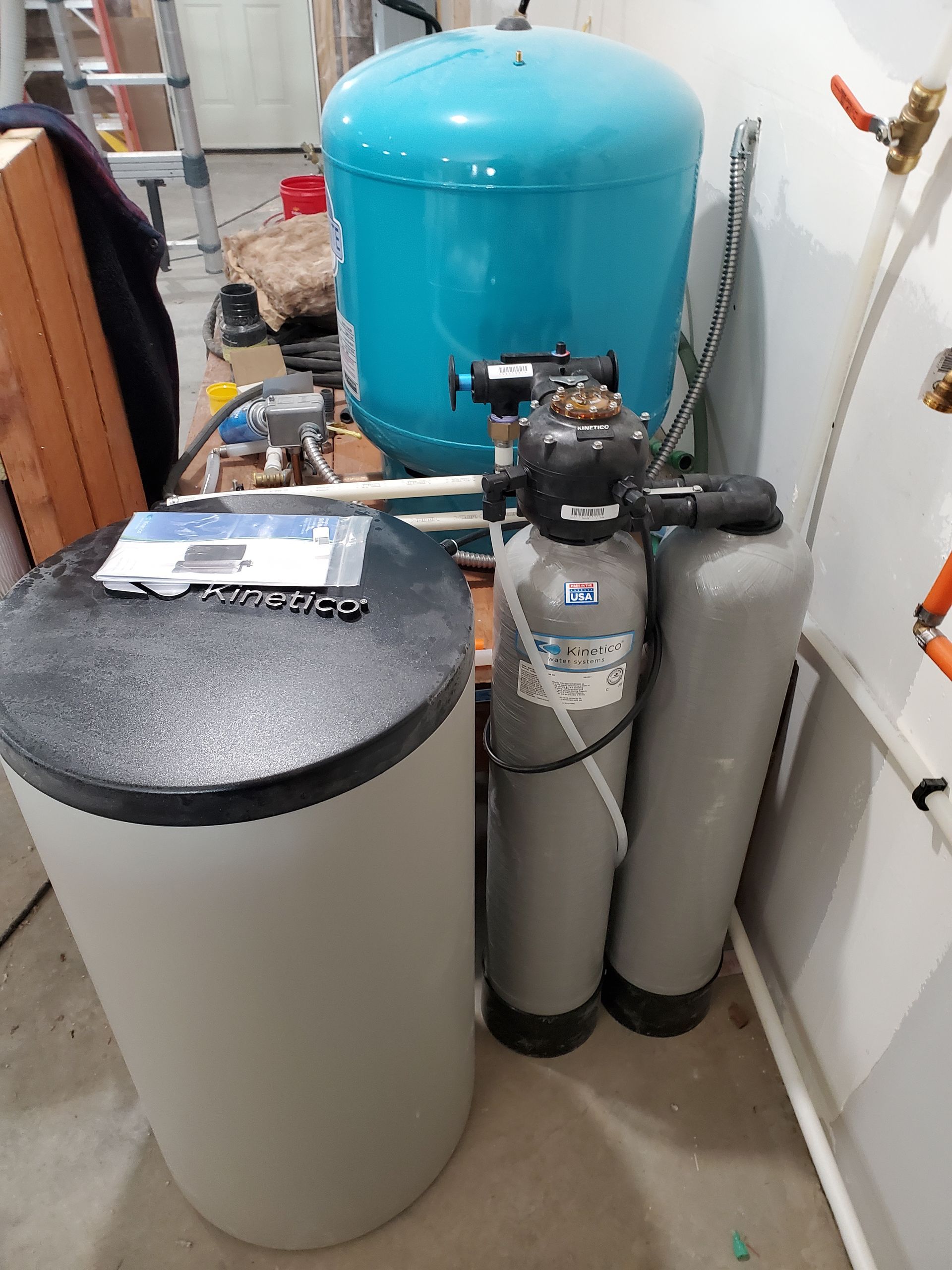 Water softener system with blue tank and white/gray cylinders in a utility room.