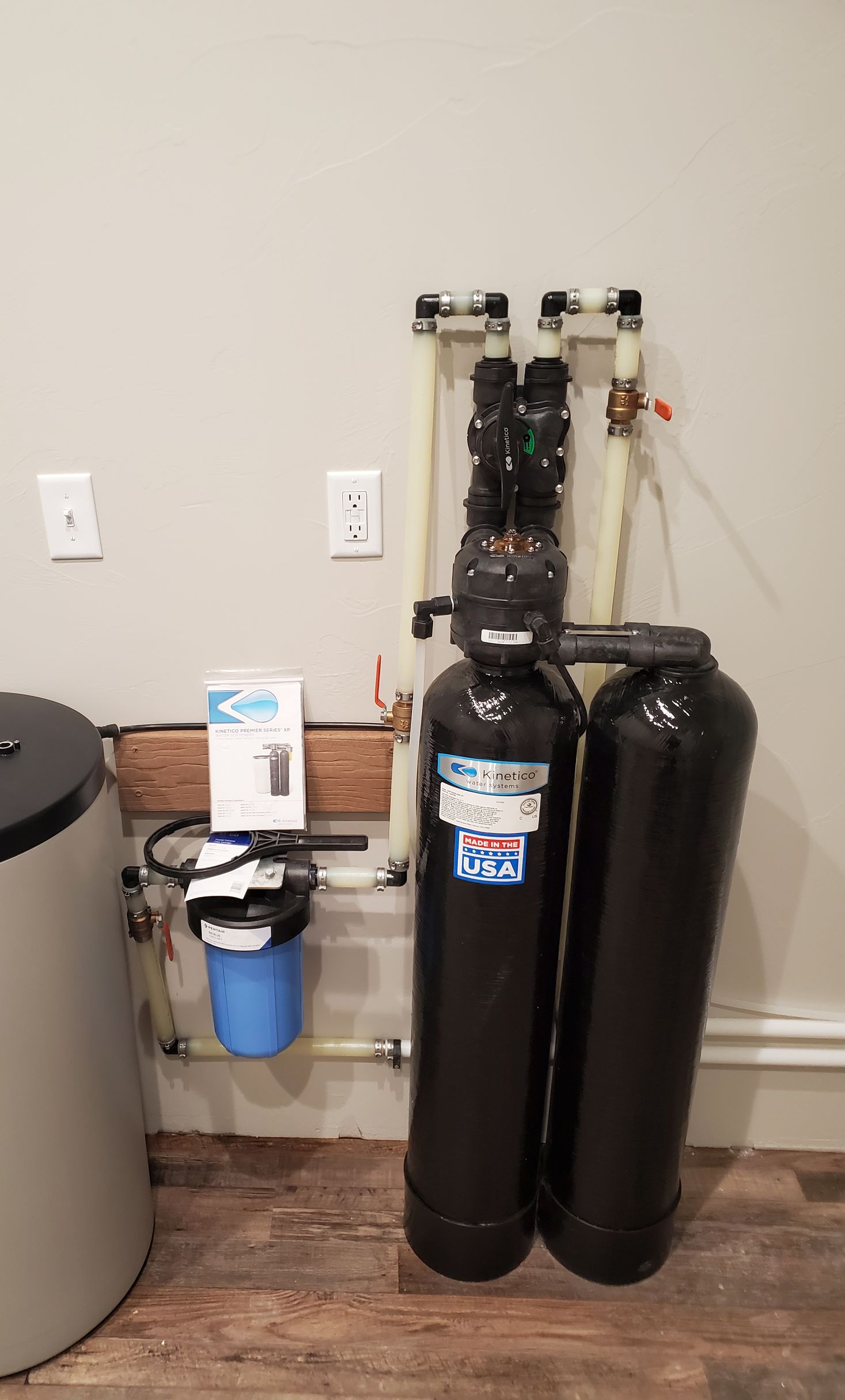 Water filtration system: two black tanks, blue filter, and pipes against a light gray wall.