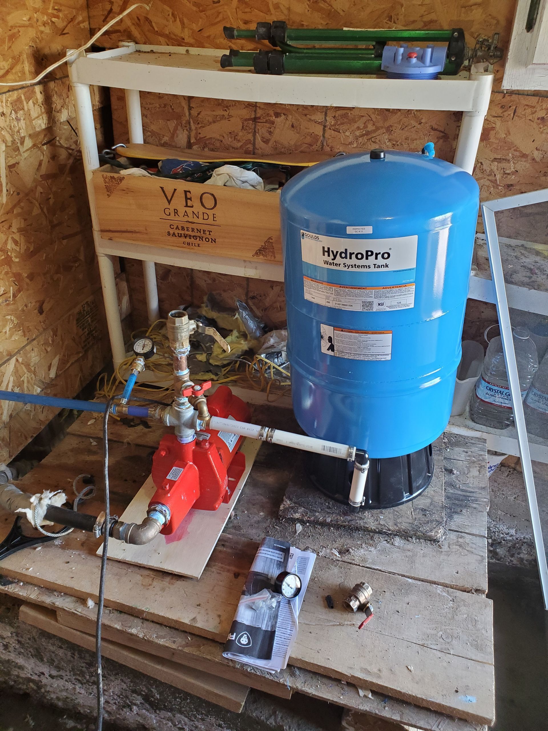 A blue water pressure tank and red pump system, indoors, with a shelf.