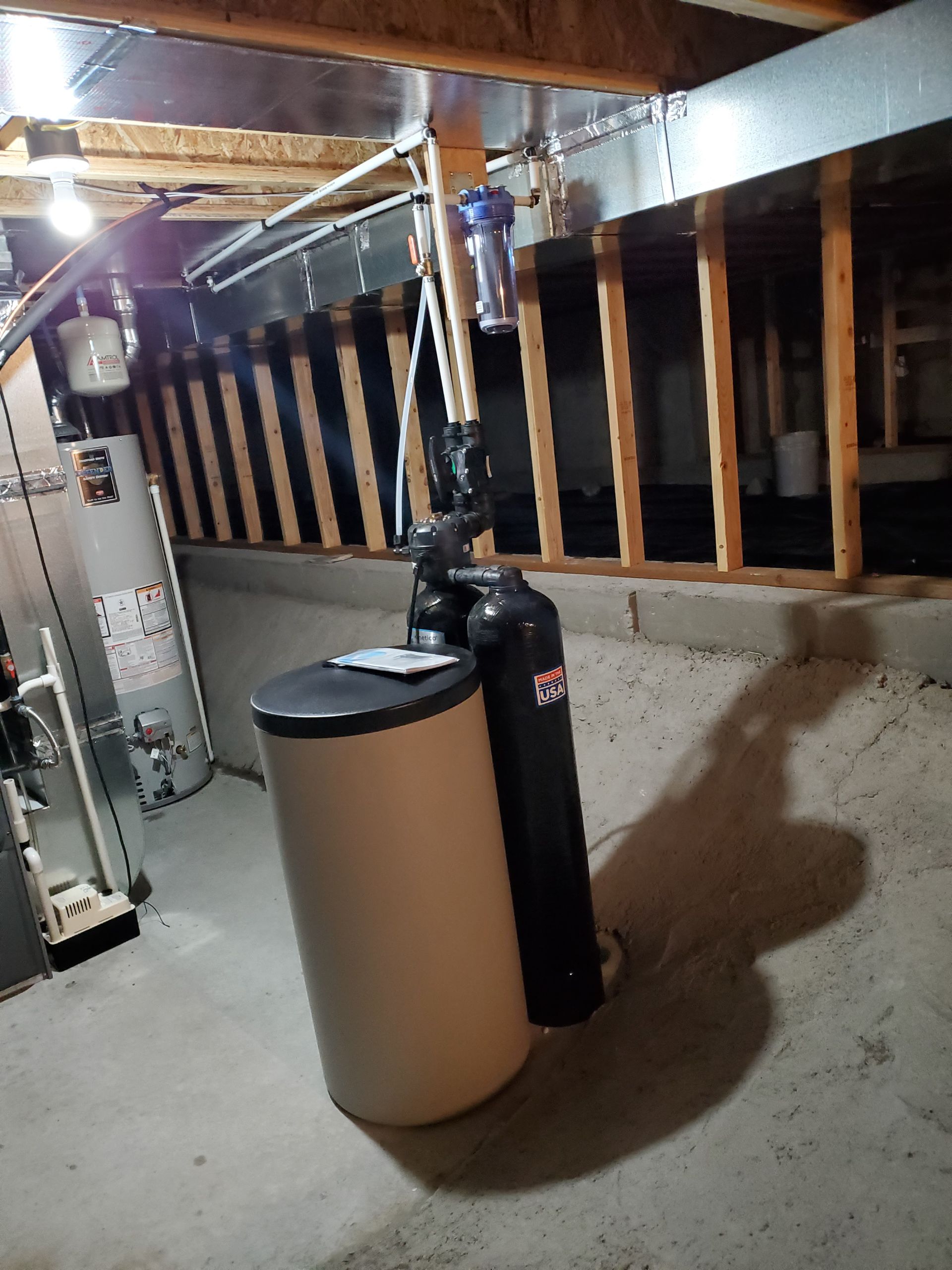 Basement with water softener system, water heater, and unfinished walls.