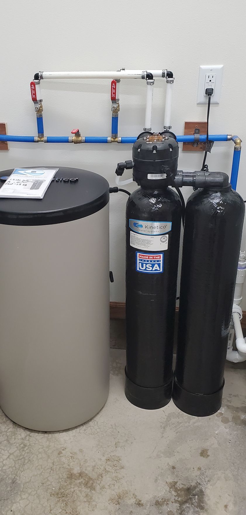 Water softener system with tanks and plumbing against a wall.