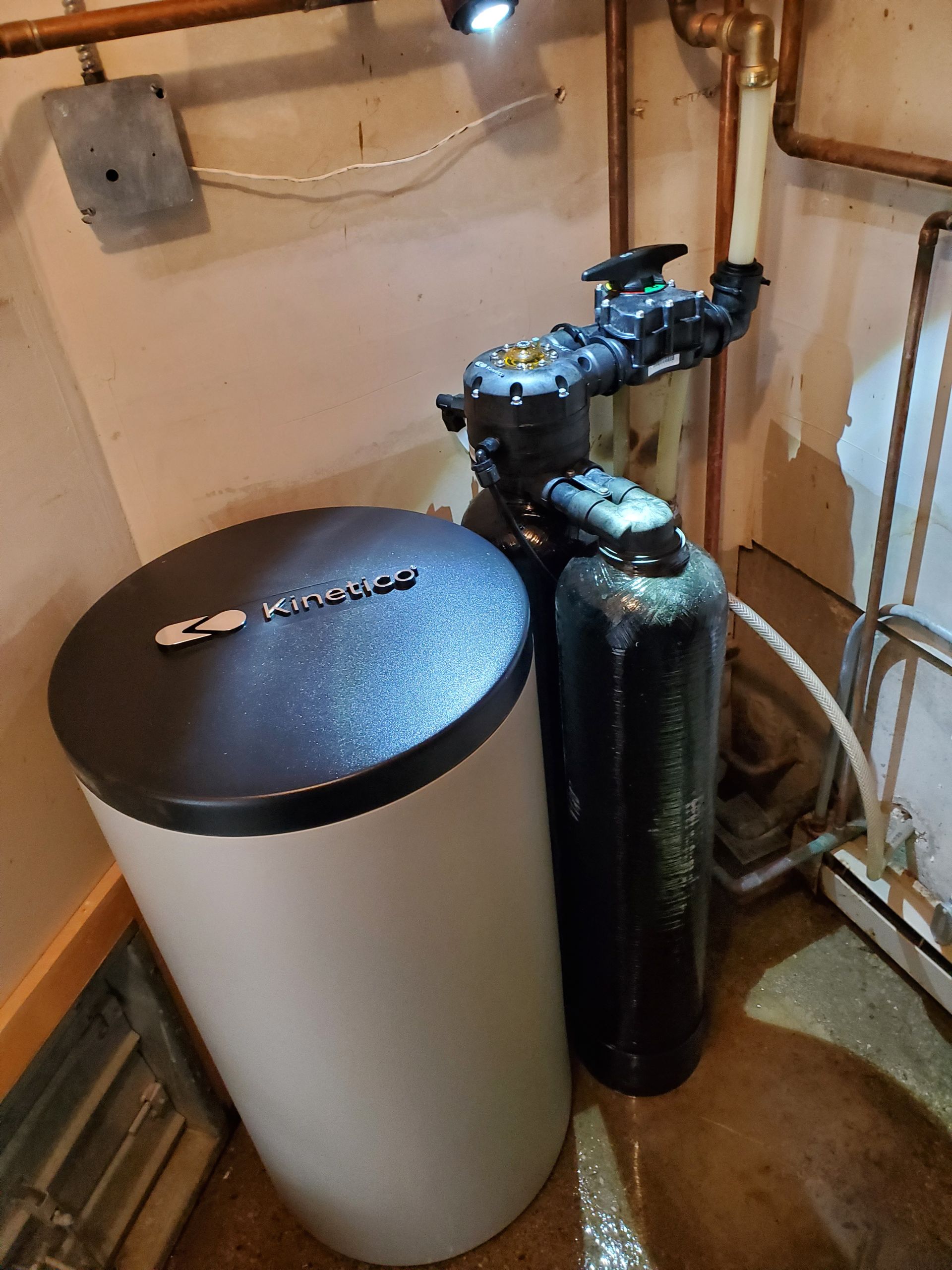 Water softener system in a basement. White tank to the left, black tank with a valve.
