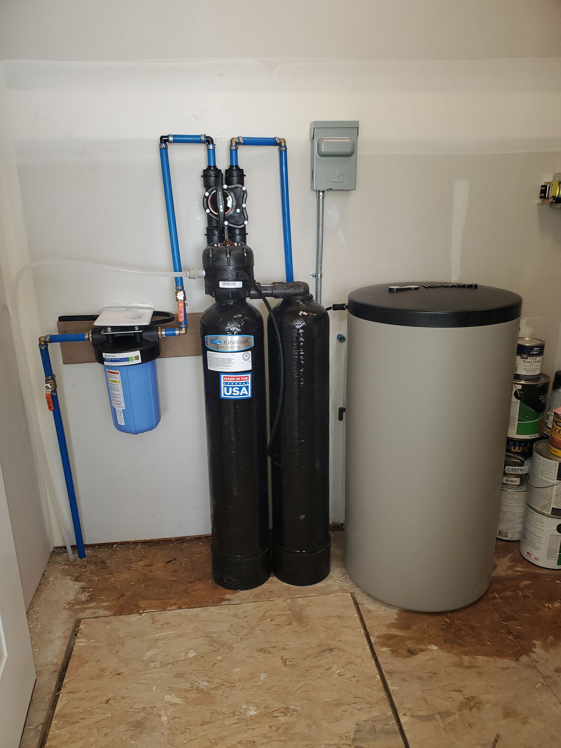 Water filtration system in a garage setting with blue pipes and a large storage tank.