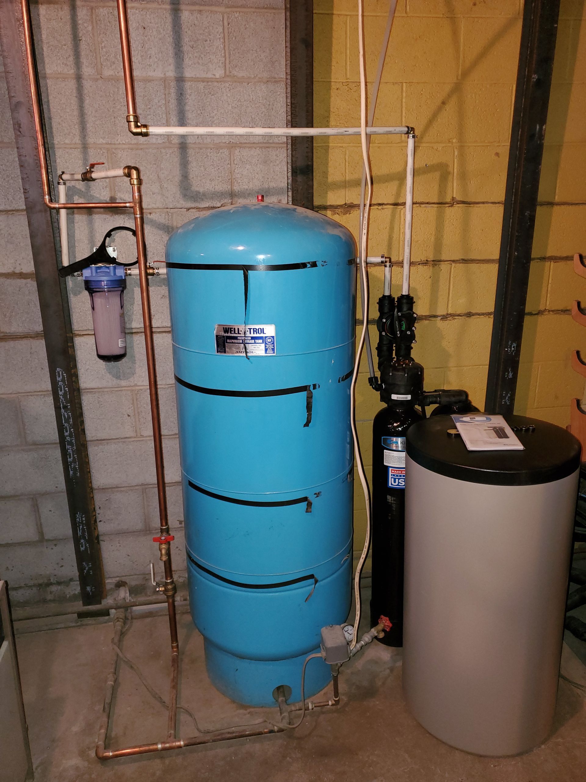 Water treatment system with blue pressure tank, filter, and softener in a basement.