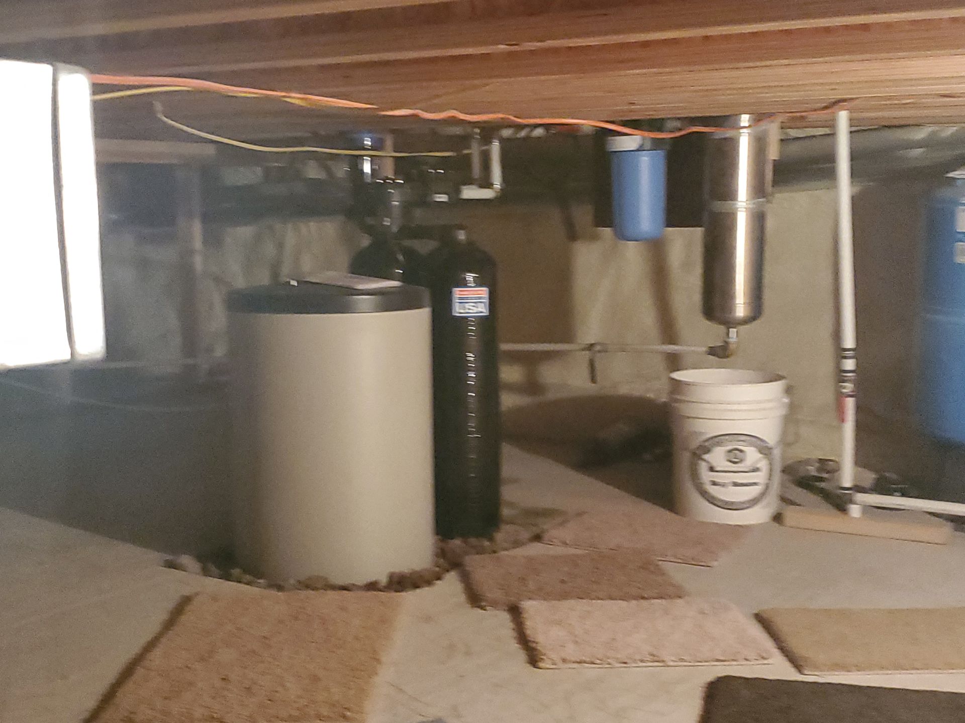 Water treatment system in a basement. Includes tanks, filters, pipes, and bucket.