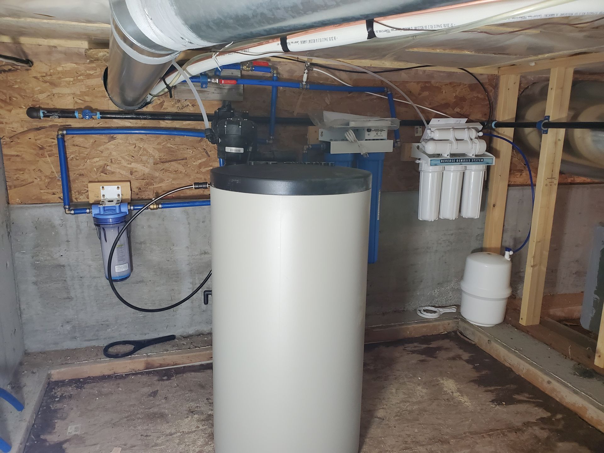 Water filtration system in a basement.  Includes a large tank, multiple filters, and associated plumbing.