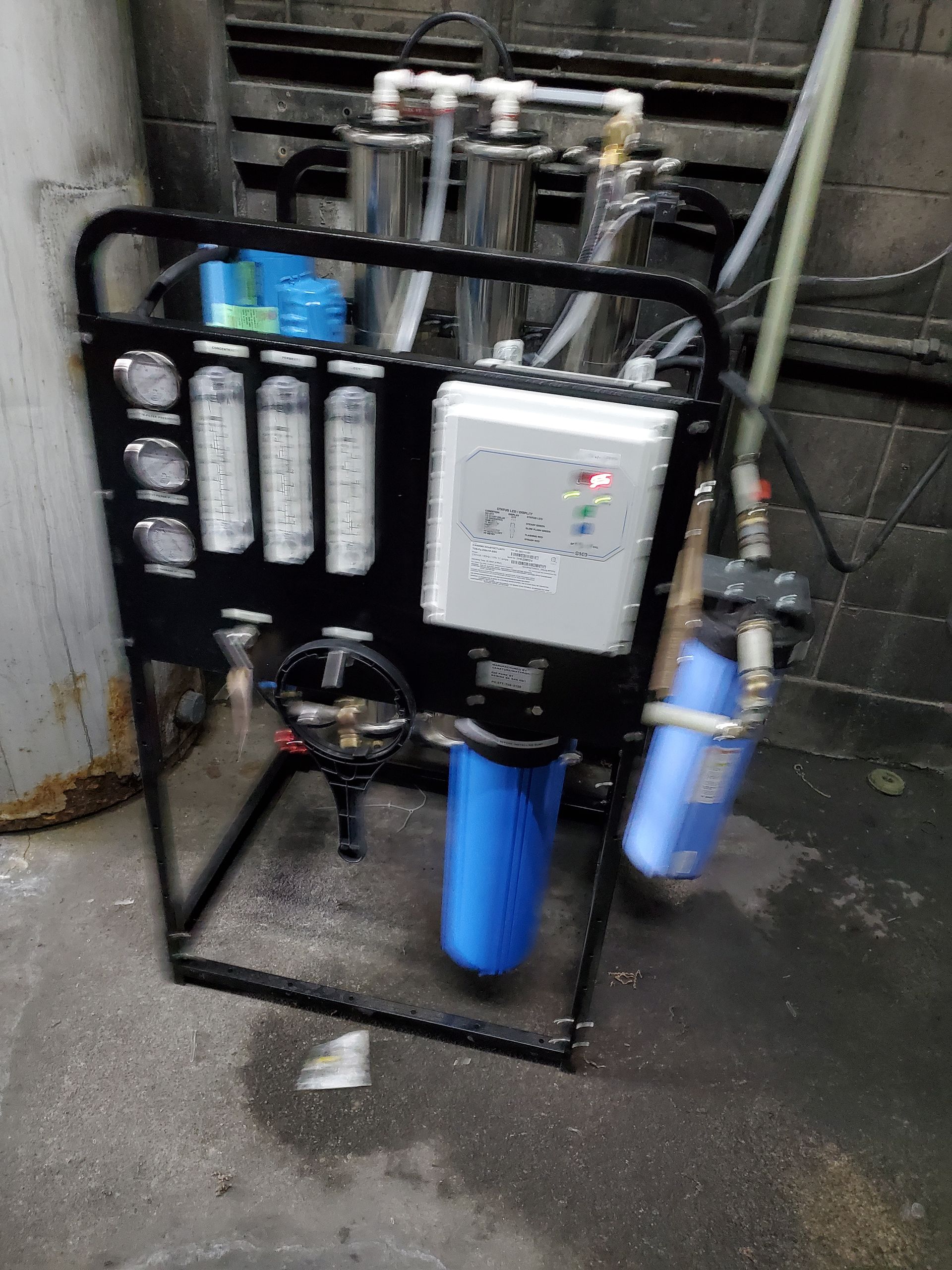 Black framed water filtration system with blue and clear filter housings, gauges, and control panel.