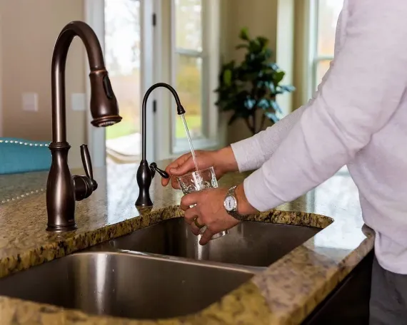 Person filling a glass with water from a kitchen faucet at a stainless steel sink.