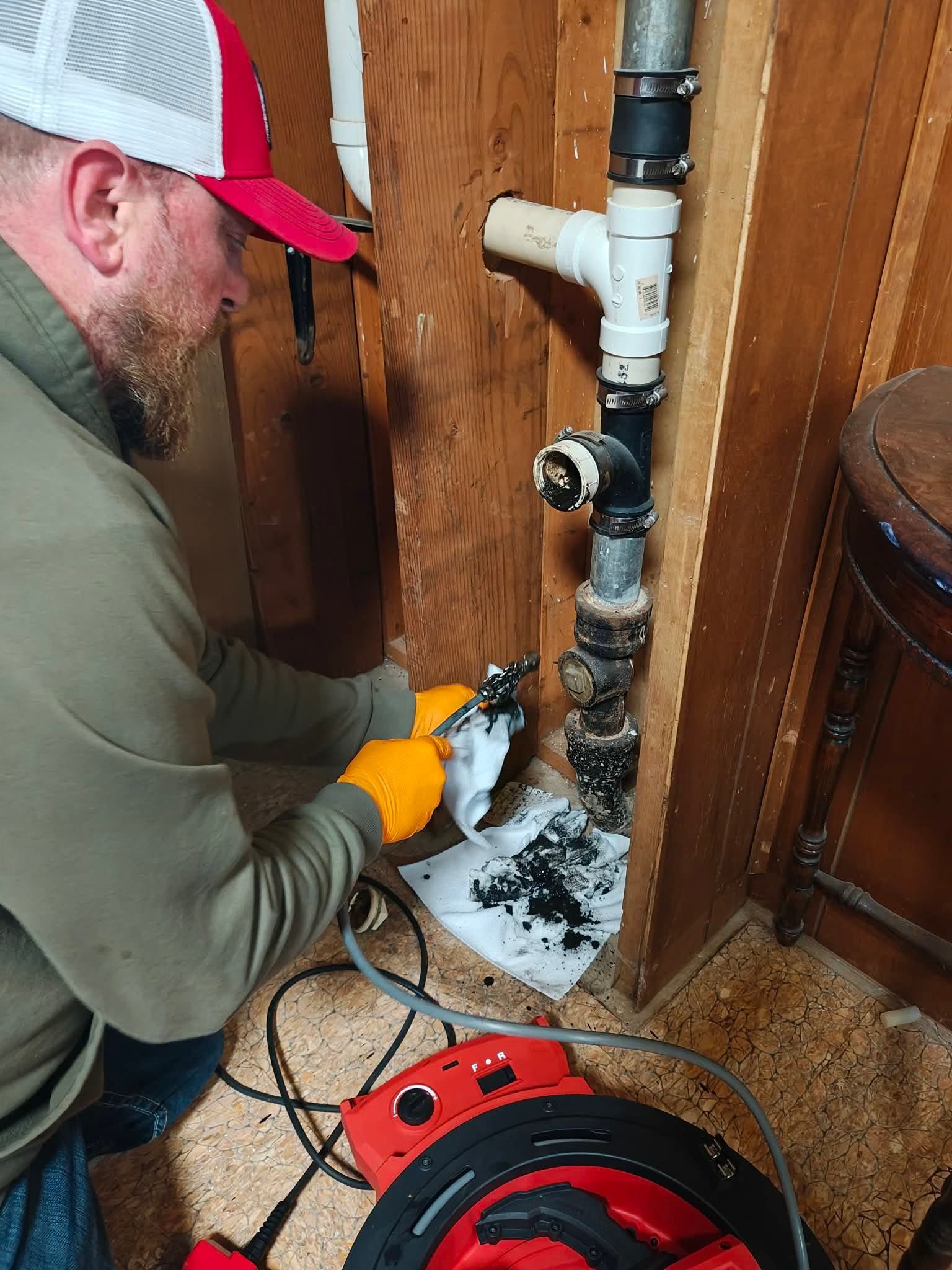 Worker using a power tool to cut a rusted pipe in a wooden-walled utility space