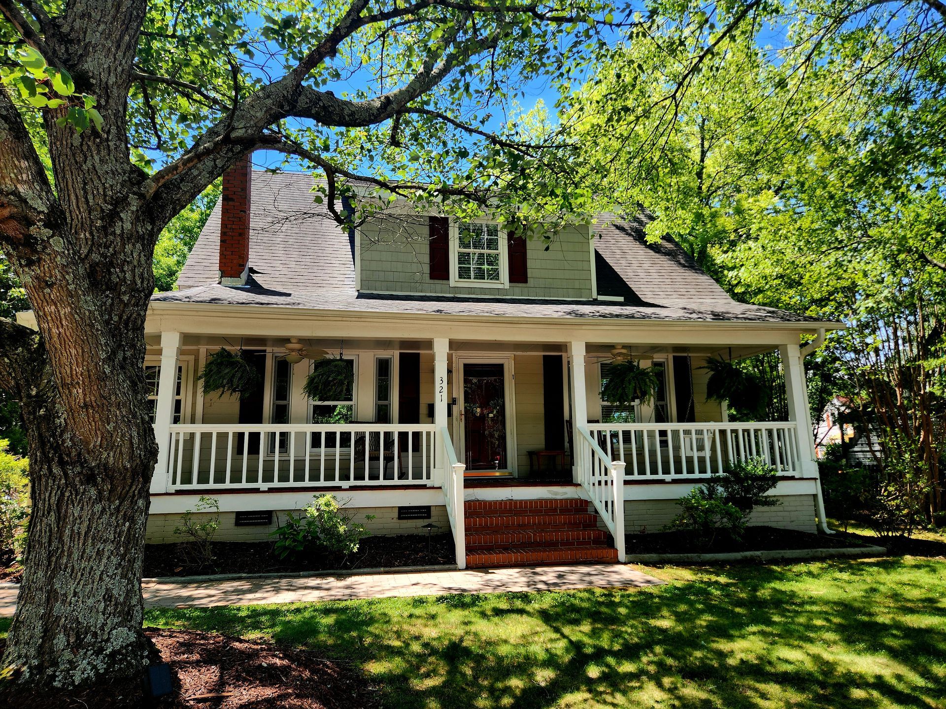 A two-story house with a porch. It has a light green exterior and a tree in the foreground.