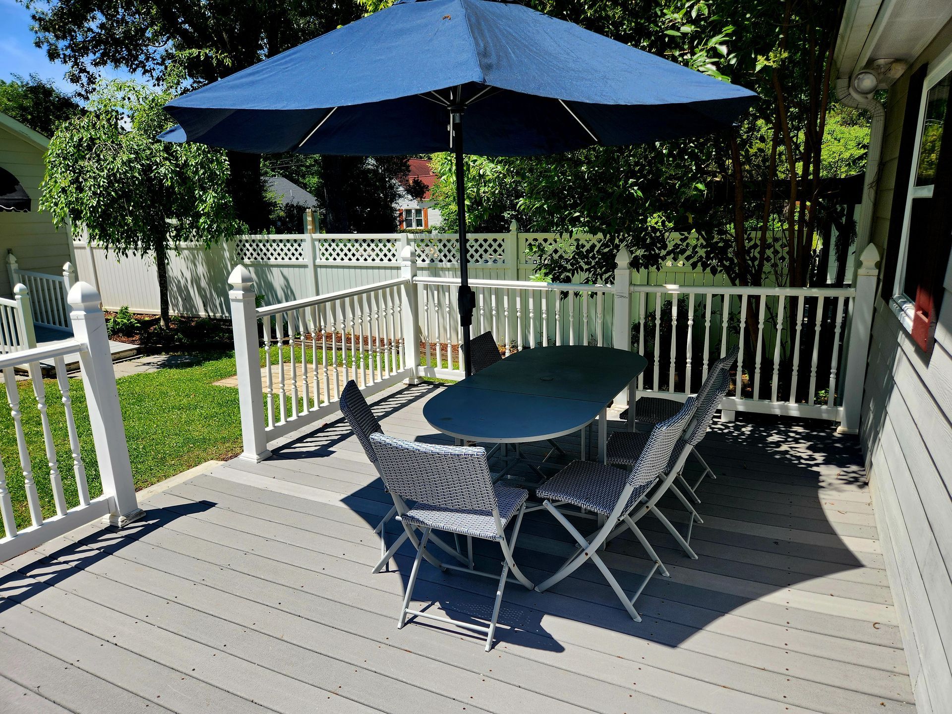 A deck with an umbrella, table, and chairs. White railing surrounds the gray deck.