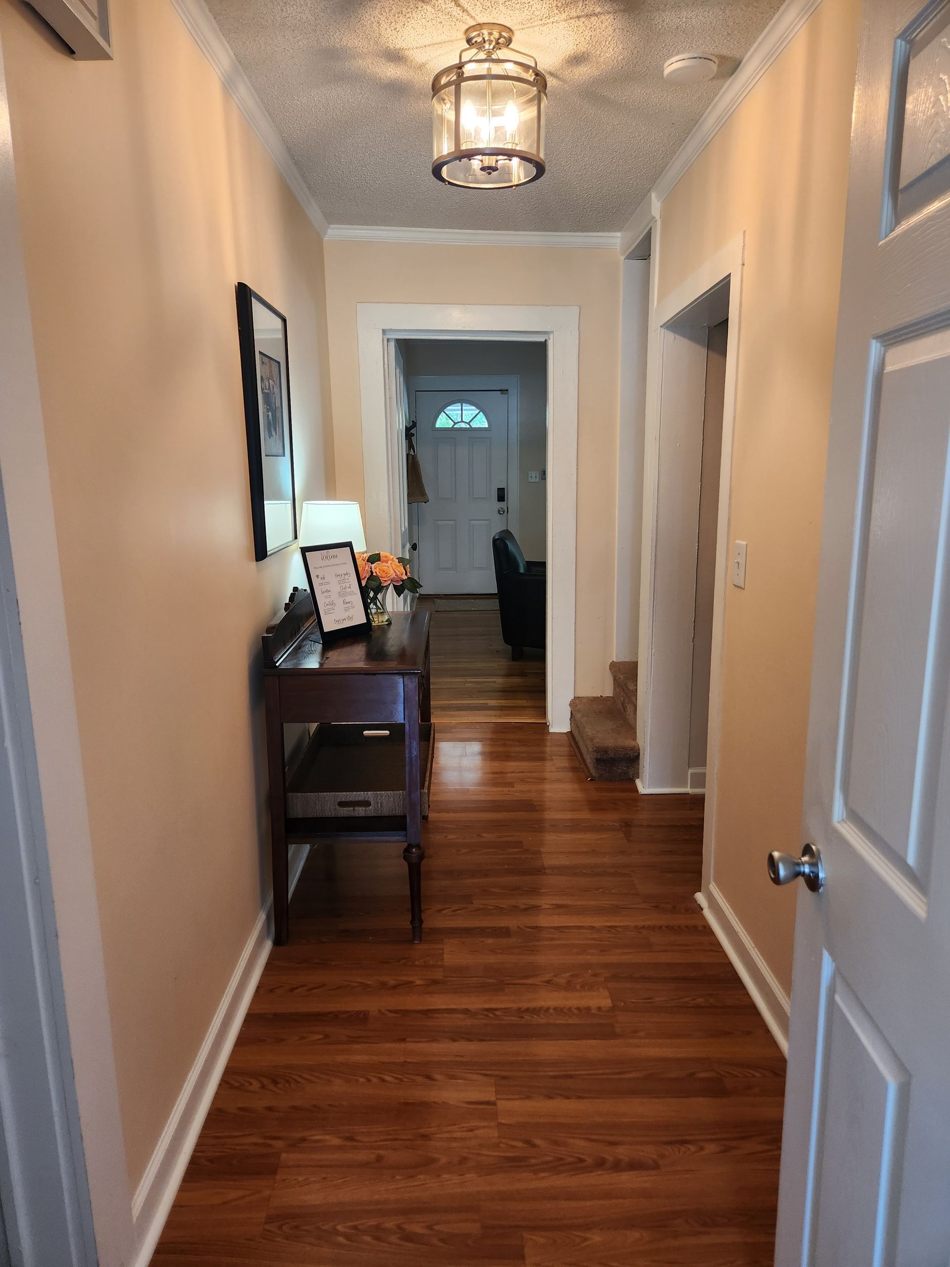 Narrow hallway with wooden floor, peach-colored walls, desk, and a door at the end.