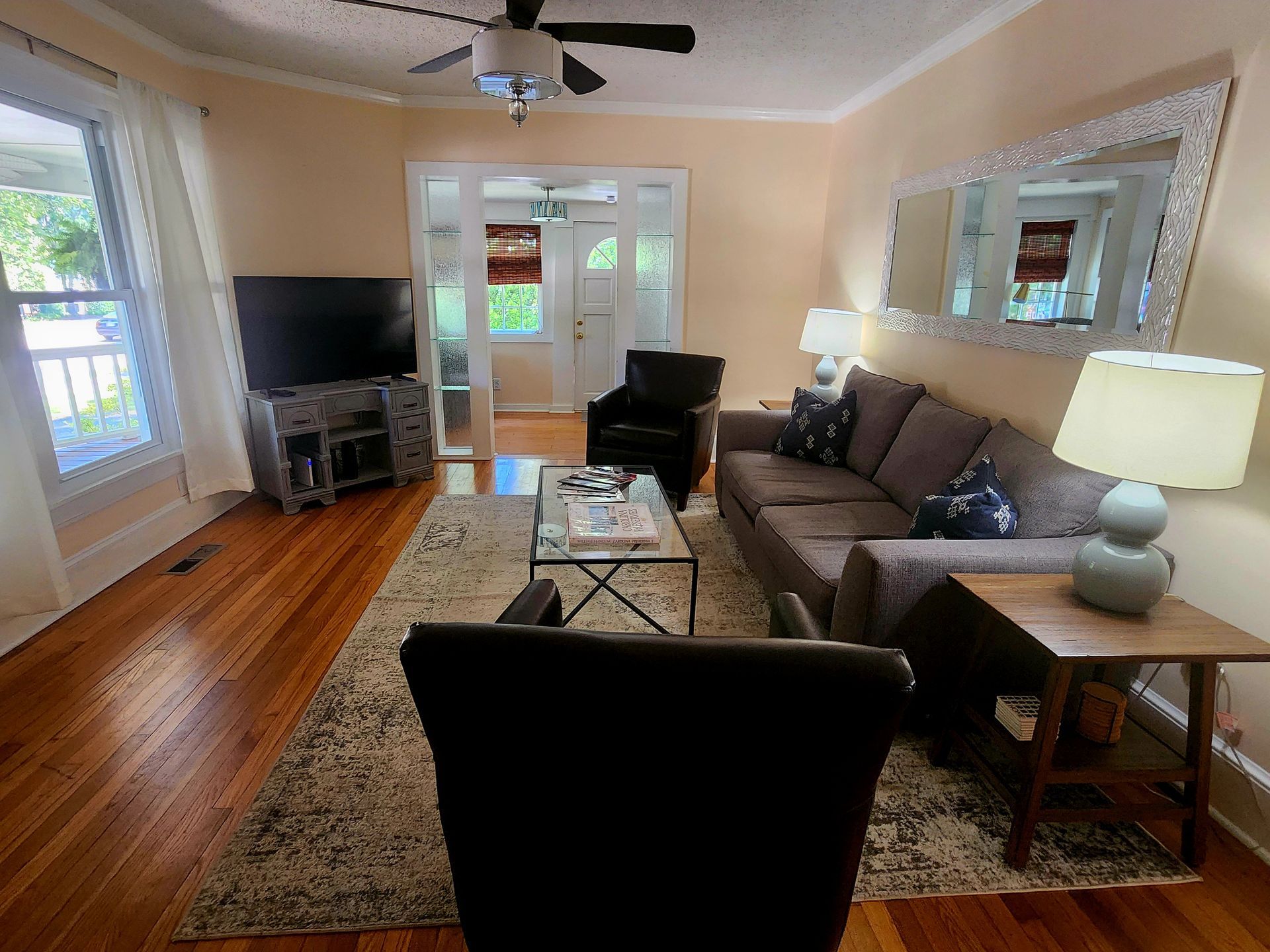 Living room with couch, TV, and coffee table; natural light, hardwood floors.