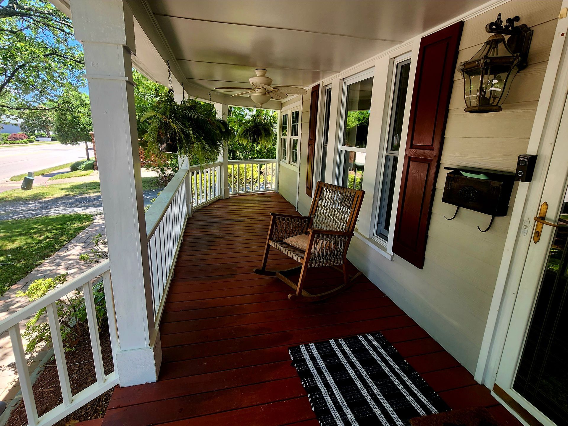 Curved front porch with rocking chair, red floor, white railing, and dark shutters.