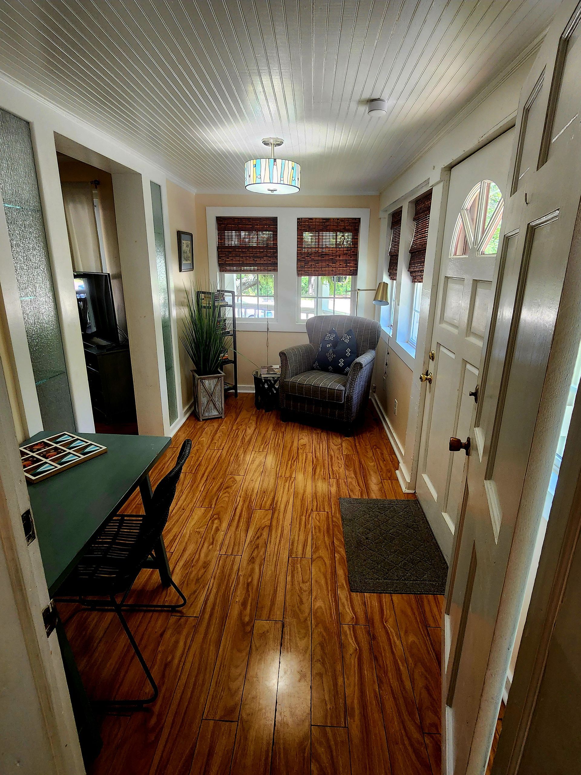 Narrow hallway with wood floors, a table on the left, a chair and windows at the end, and a door on the right.
