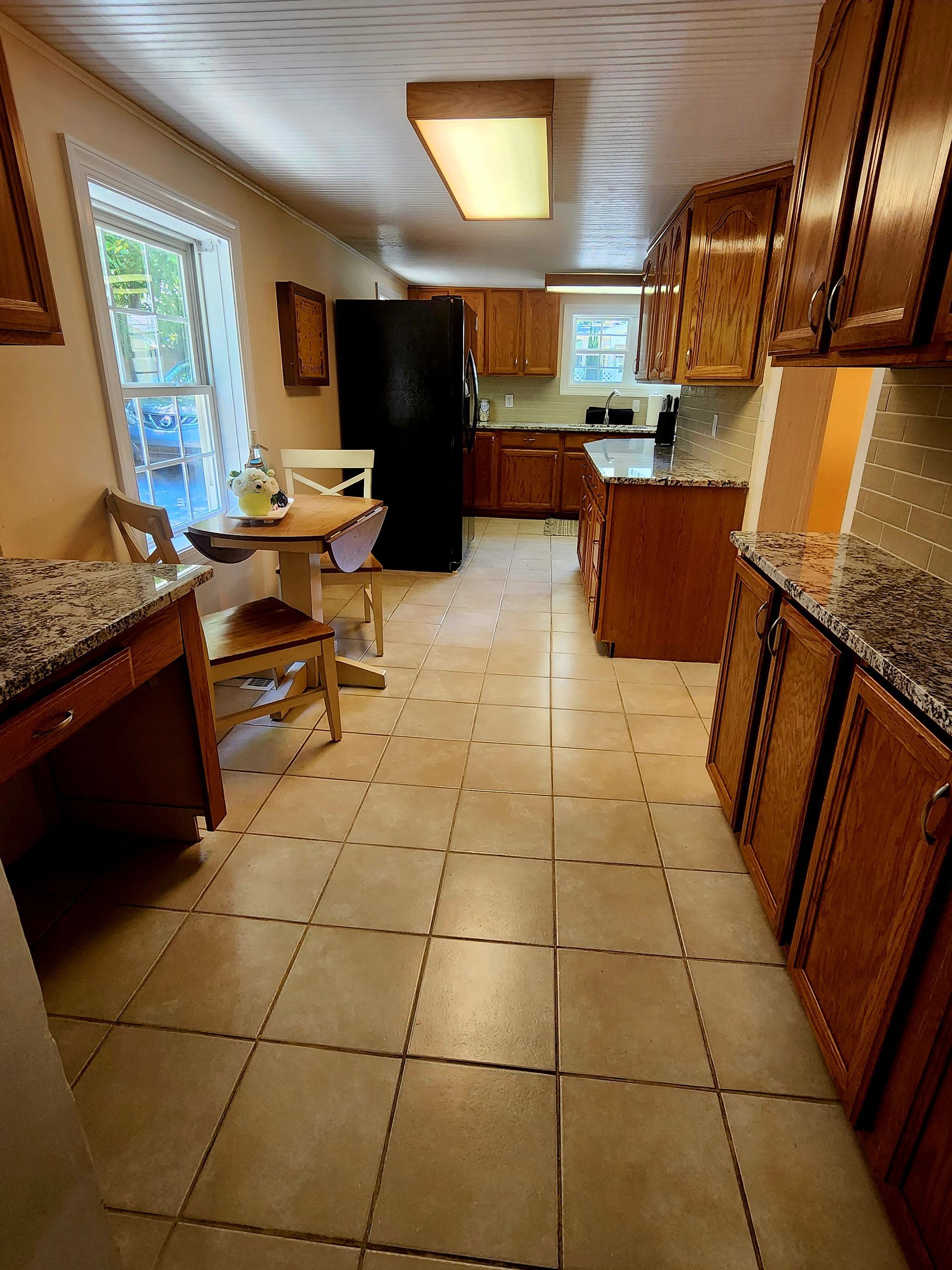 Kitchen with wooden cabinets, black fridge, small table, and tile floor.