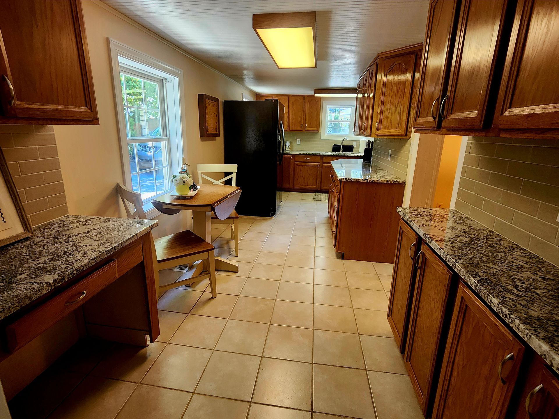 Kitchen with wooden cabinets, granite countertops, and tile floor; small table by window.