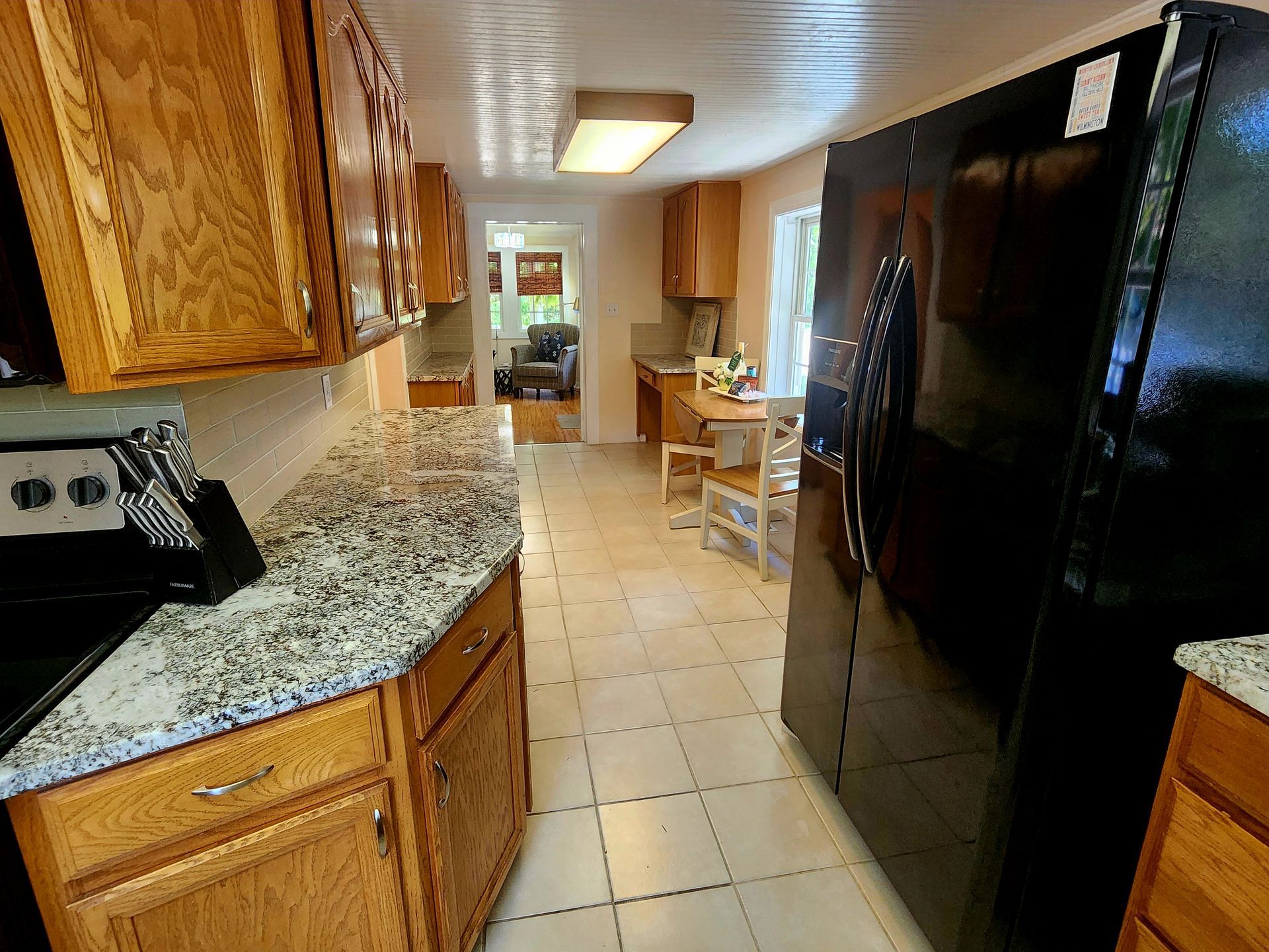 Kitchen with wood cabinets, black refrigerator, and light-colored tile floor. View extends to dining area.