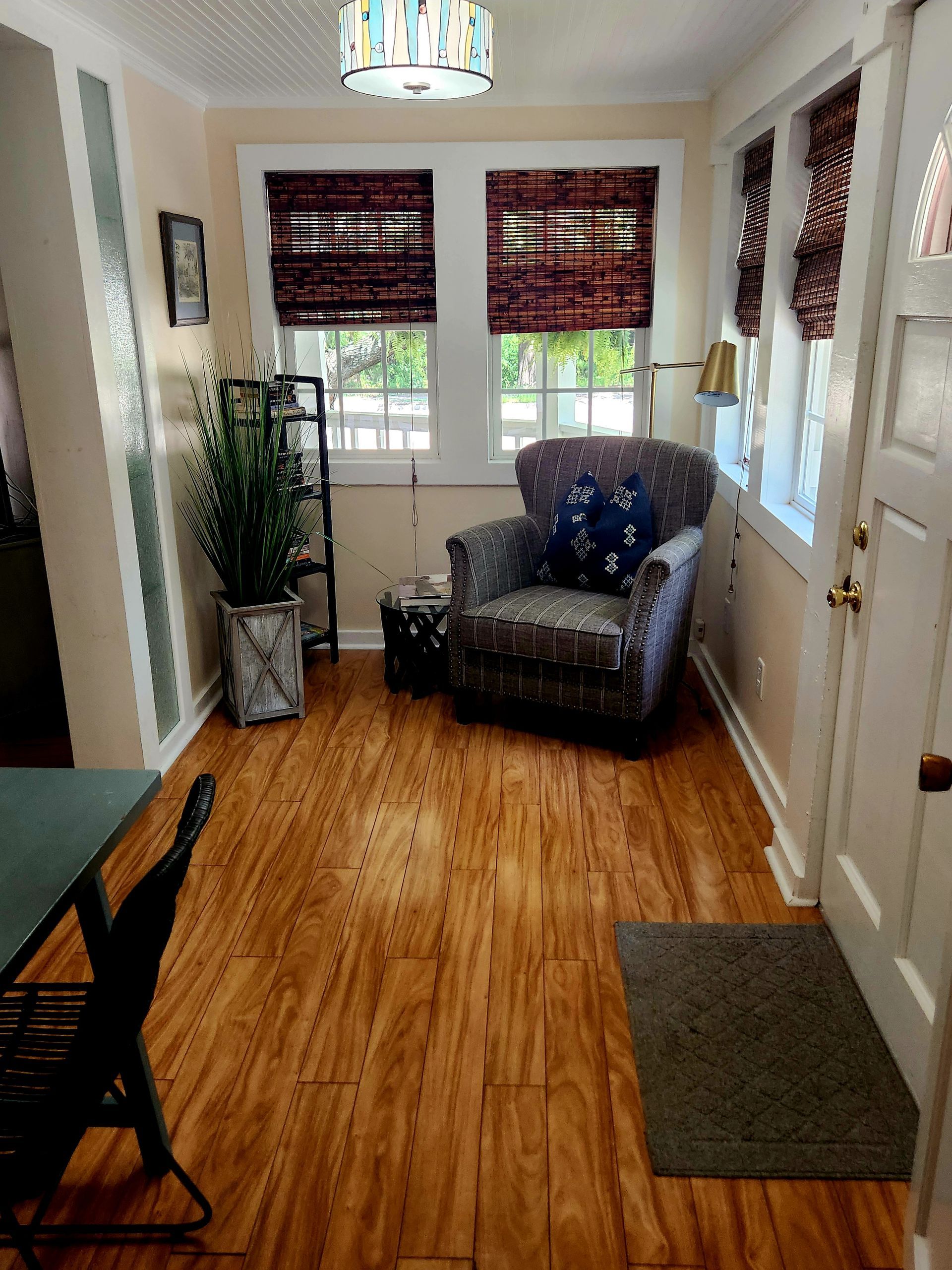 Sunroom with patterned armchair, two windows with blinds, and bamboo flooring.