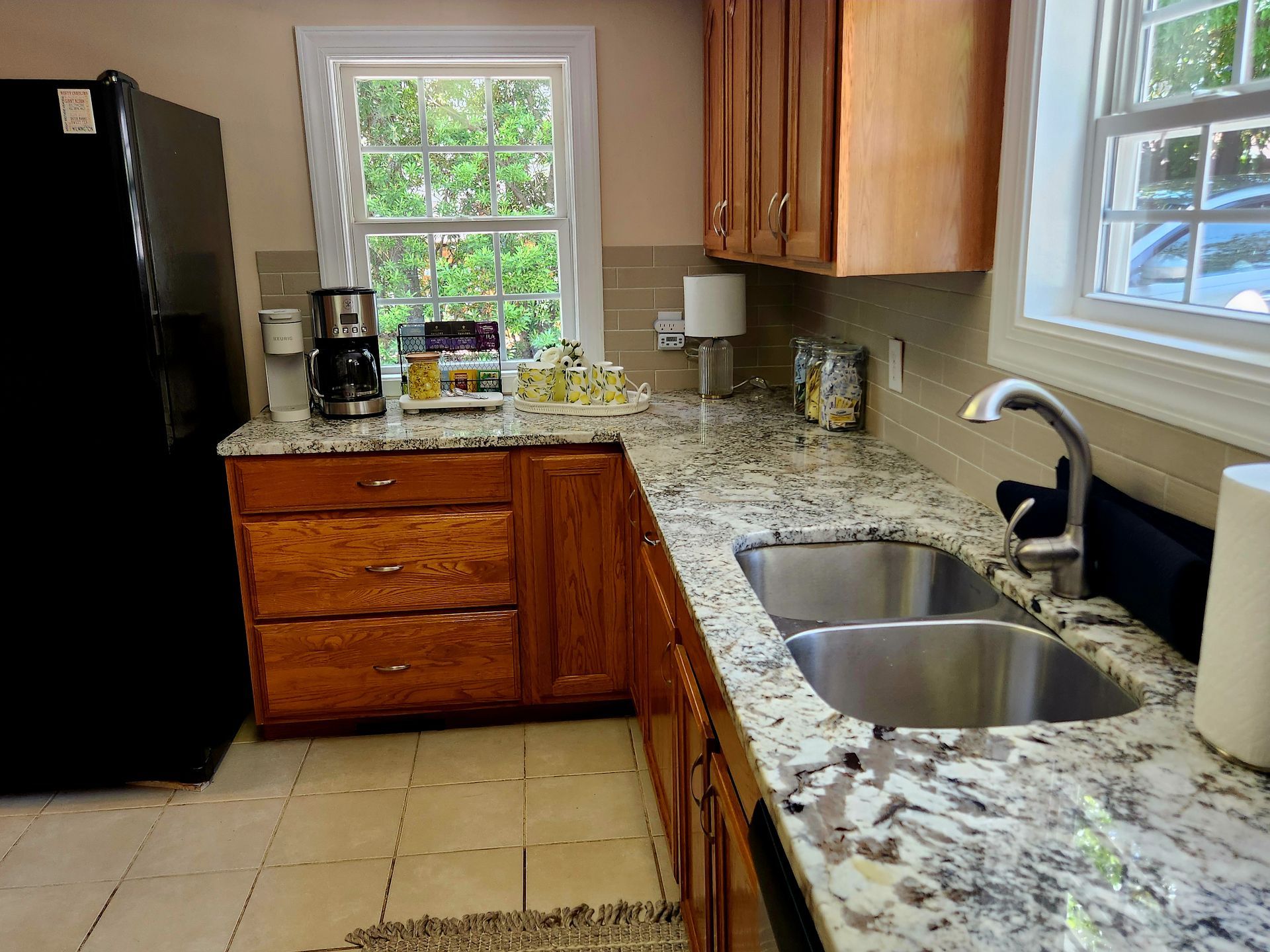 Kitchen with wood cabinets, granite countertops, and a double sink. Black refrigerator and windows visible.