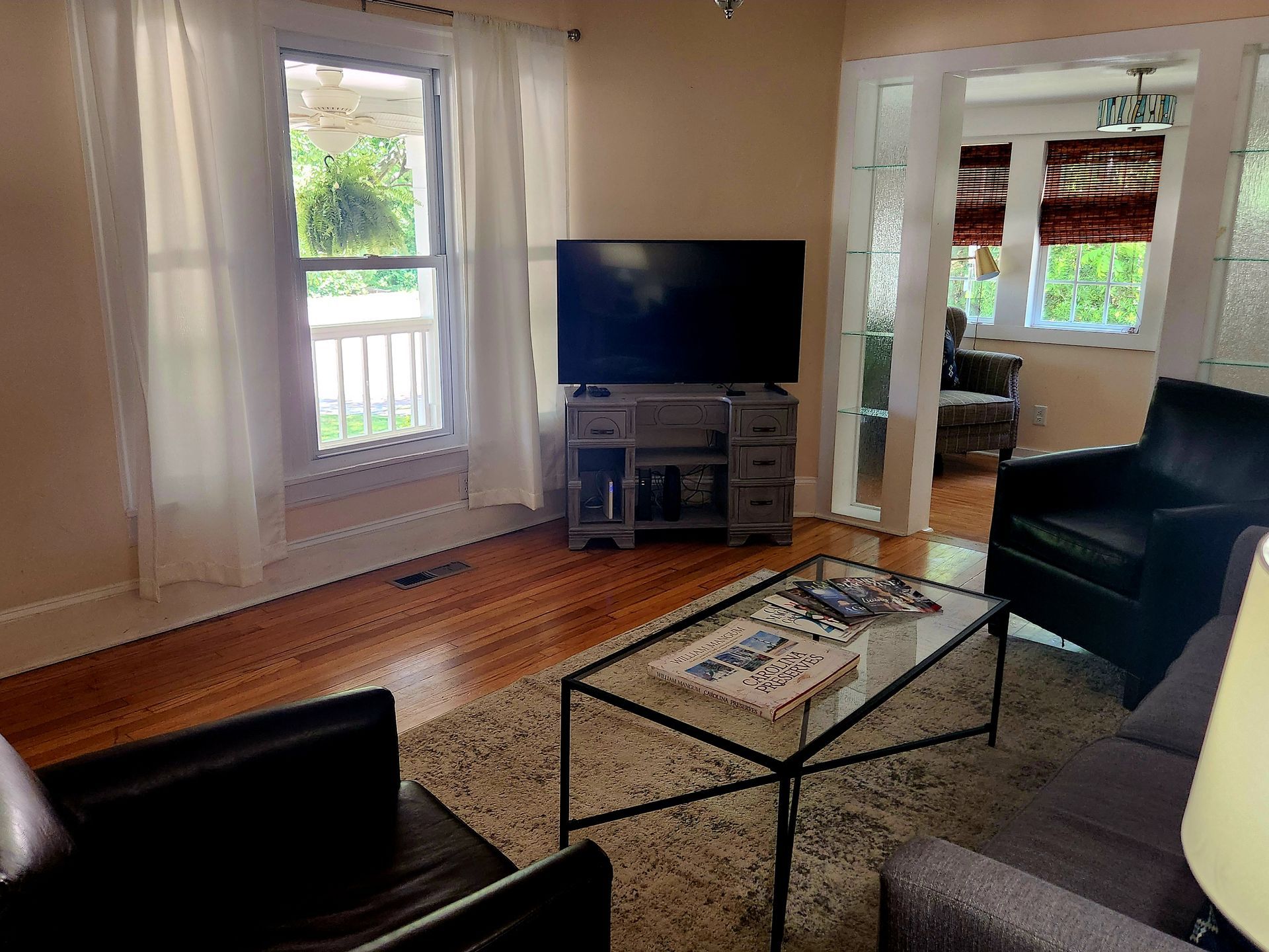 Living room with hardwood floors, a TV, a glass coffee table, and an open doorway to another room.