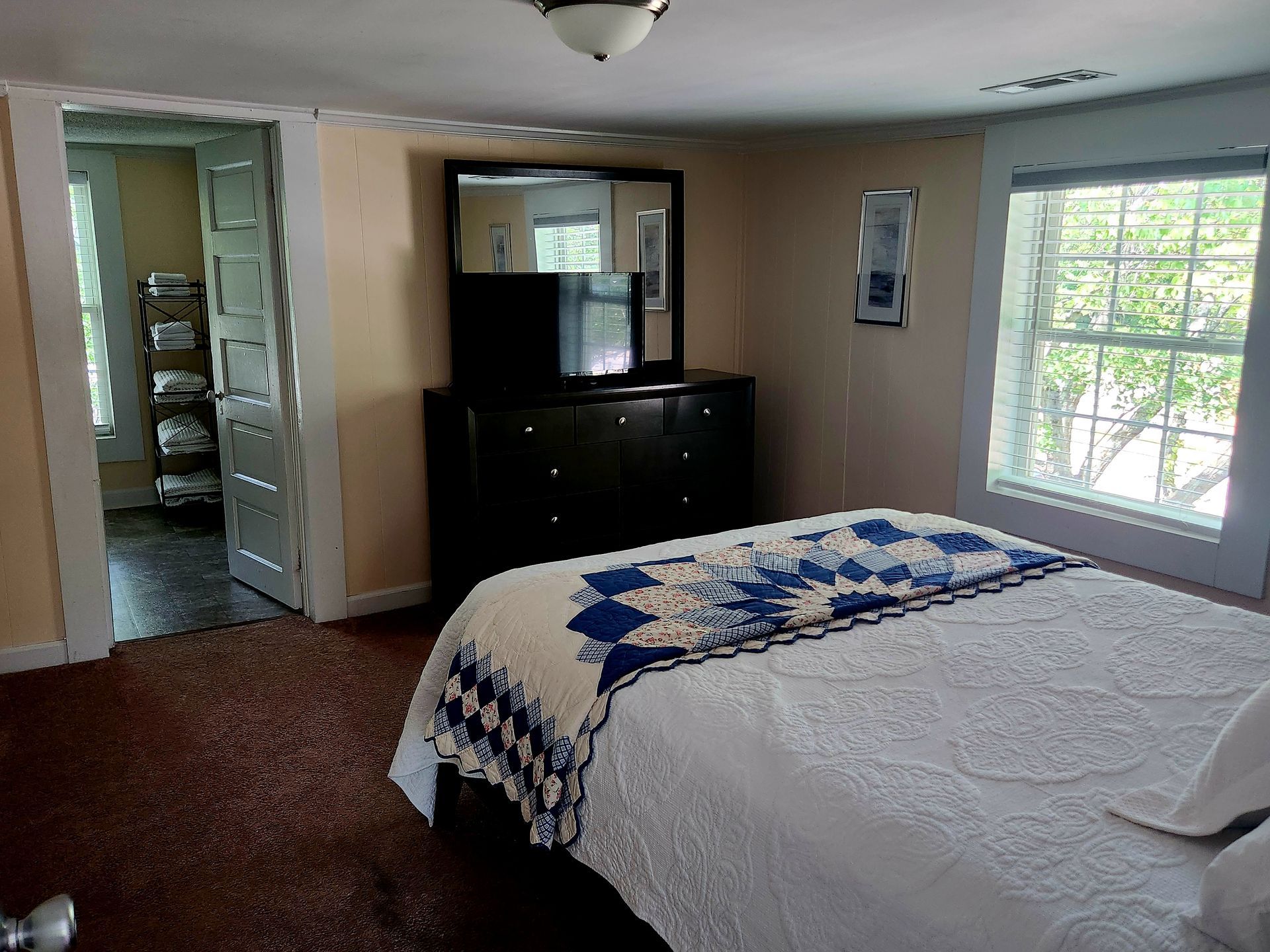Bedroom with bed, dresser, mirror, window, and doorway to another room.