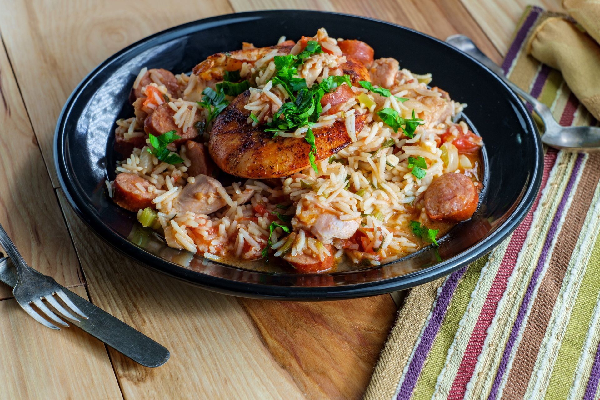 Rice dish with sausage, tomatoes, and herbs in a black bowl on a wooden table.