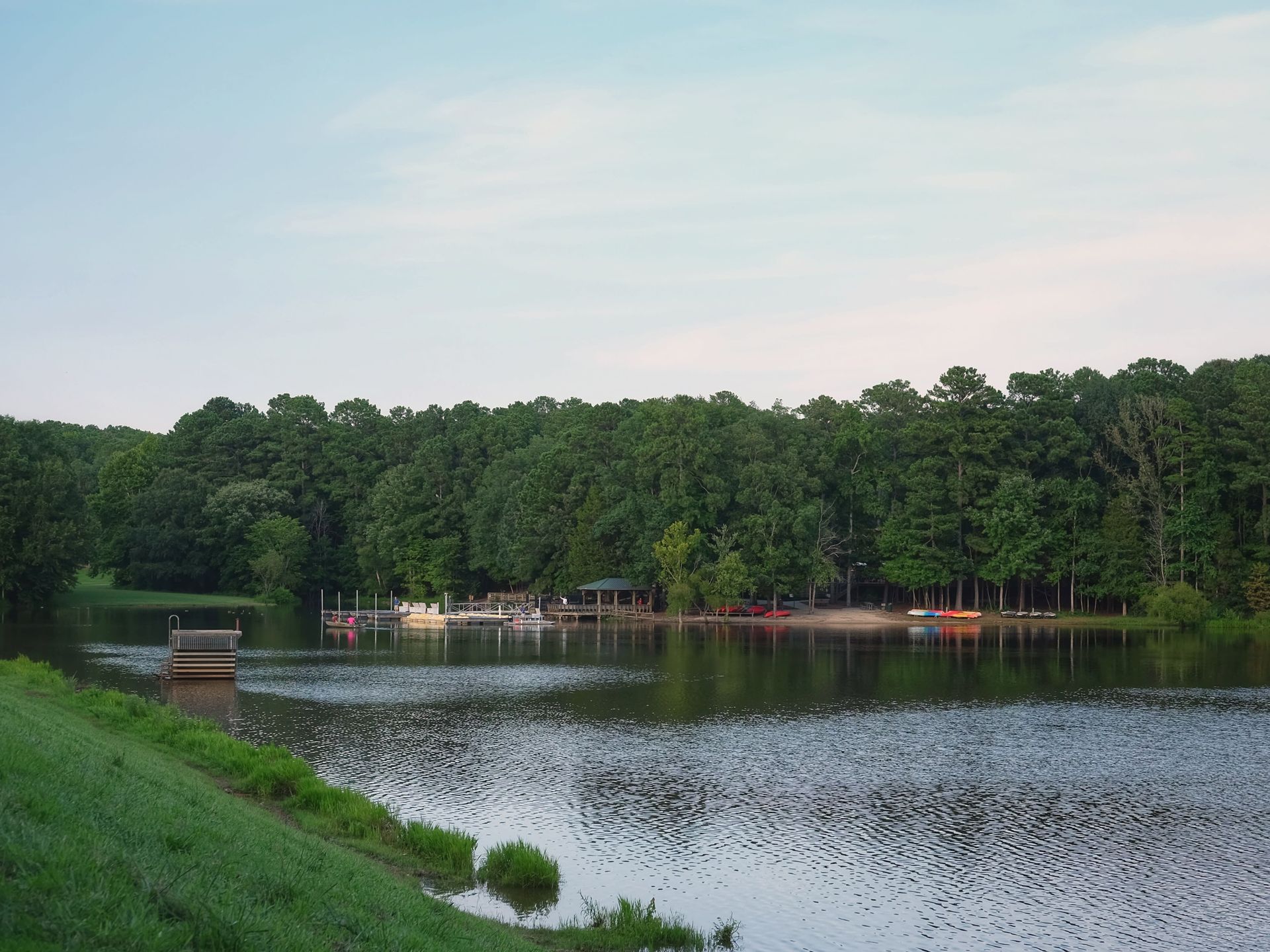 Lakeside view with green trees, calm water, and a wooden dock.
