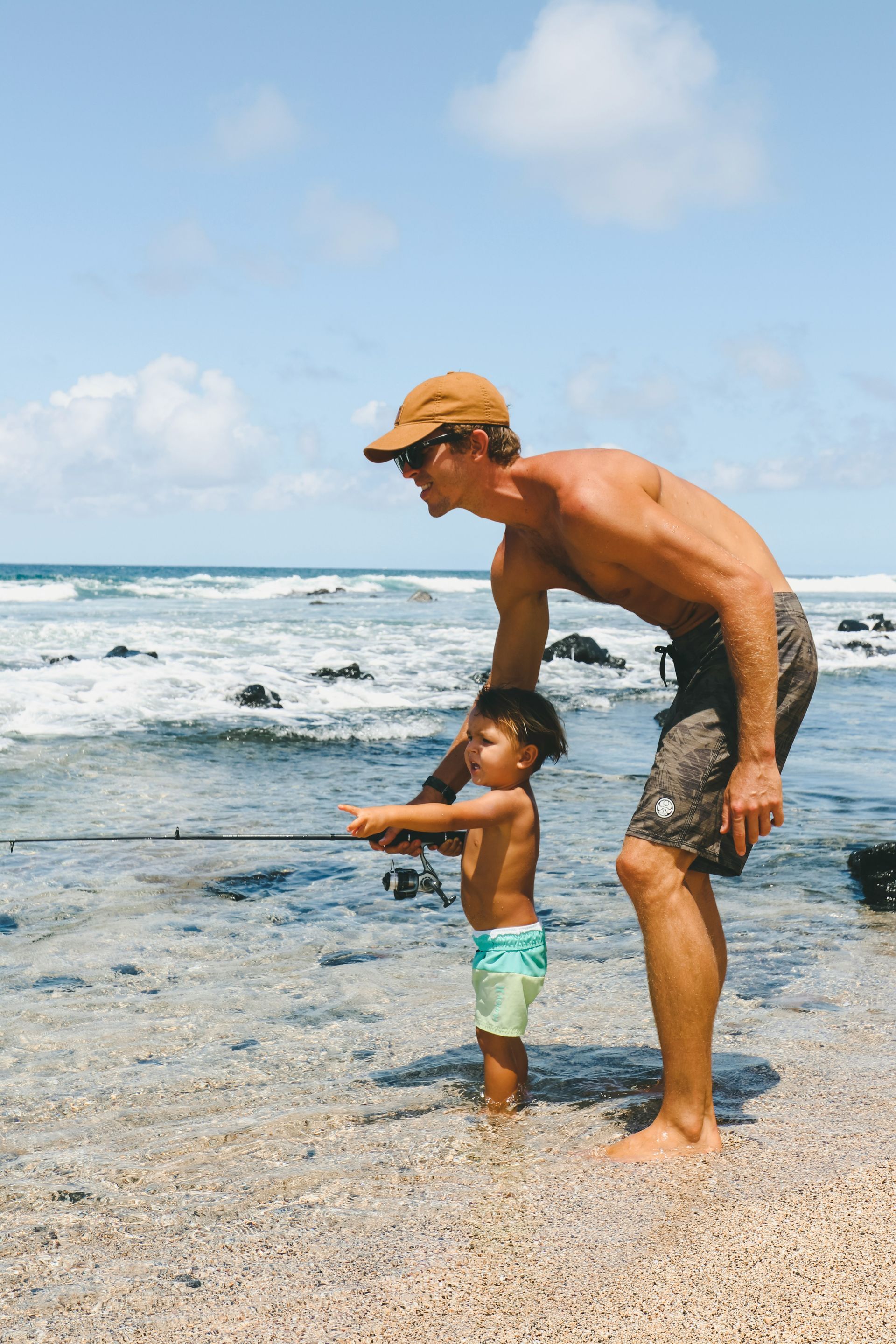 A man is teaching a little boy how to fish on the beach.