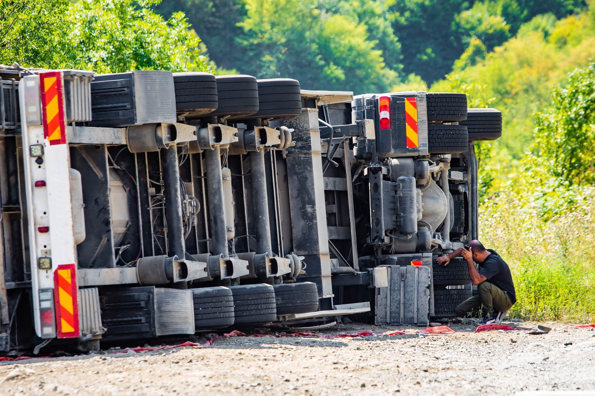 Large cargo truck turned over on the side of a road after an accident. The driver is besides it.