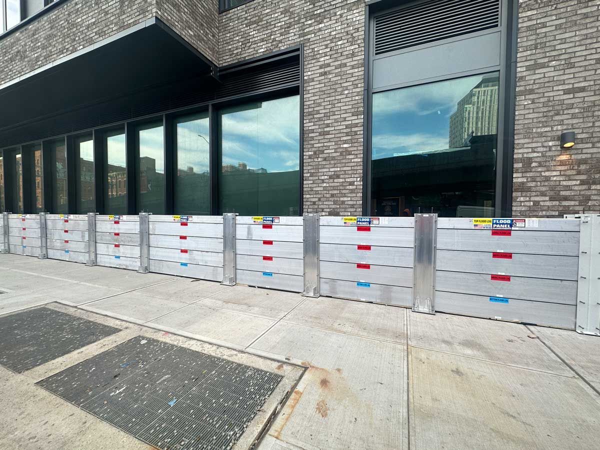 A row of flood barriers are sitting on the sidewalk in front of a brick building.