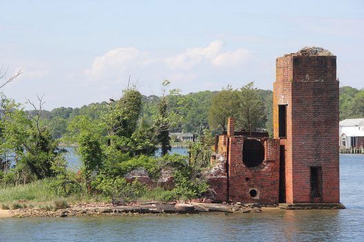 A brick building is sitting on top of a small island in the middle of a body of water.