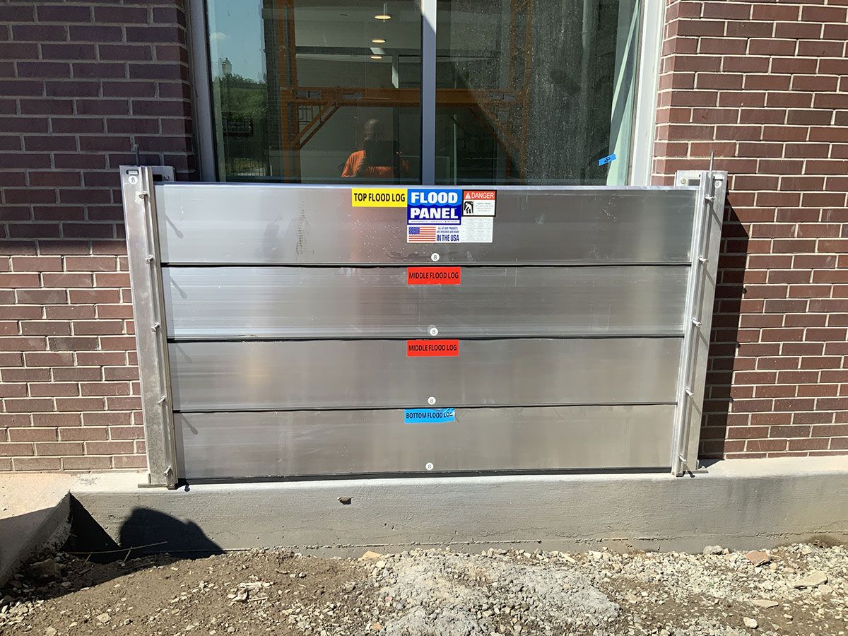 A stainless steel flood barrier is sitting in front of a brick building.