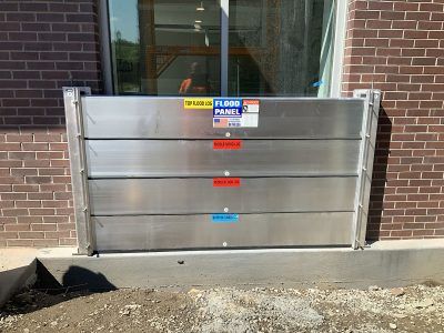 A stainless steel flood barrier is sitting on the side of a brick building.