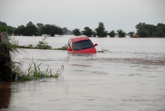 A red car is stuck in a flooded field.