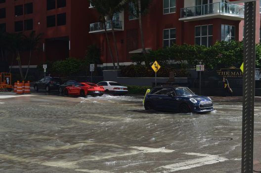 A blue car is driving through a flooded intersection