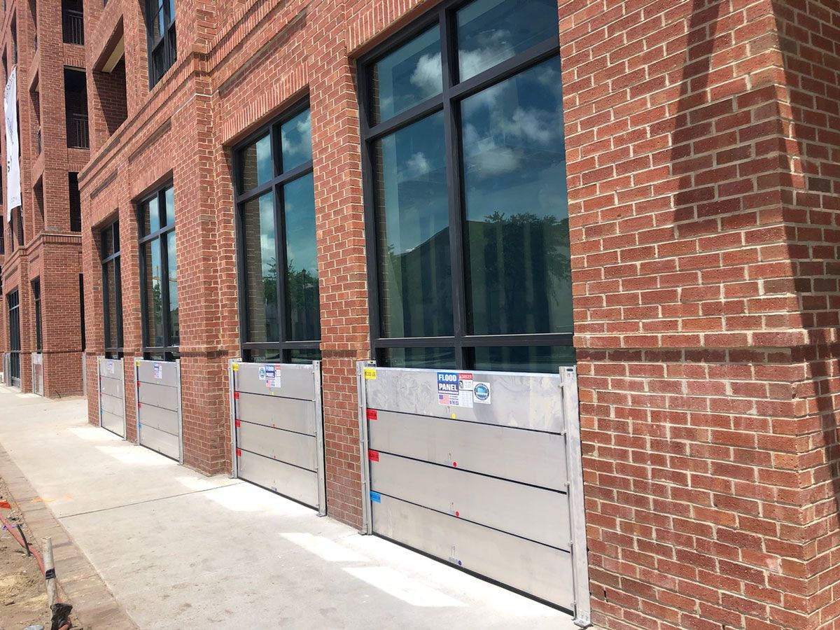 A brick building with a lot of windows and flood barriers on the sidewalk.