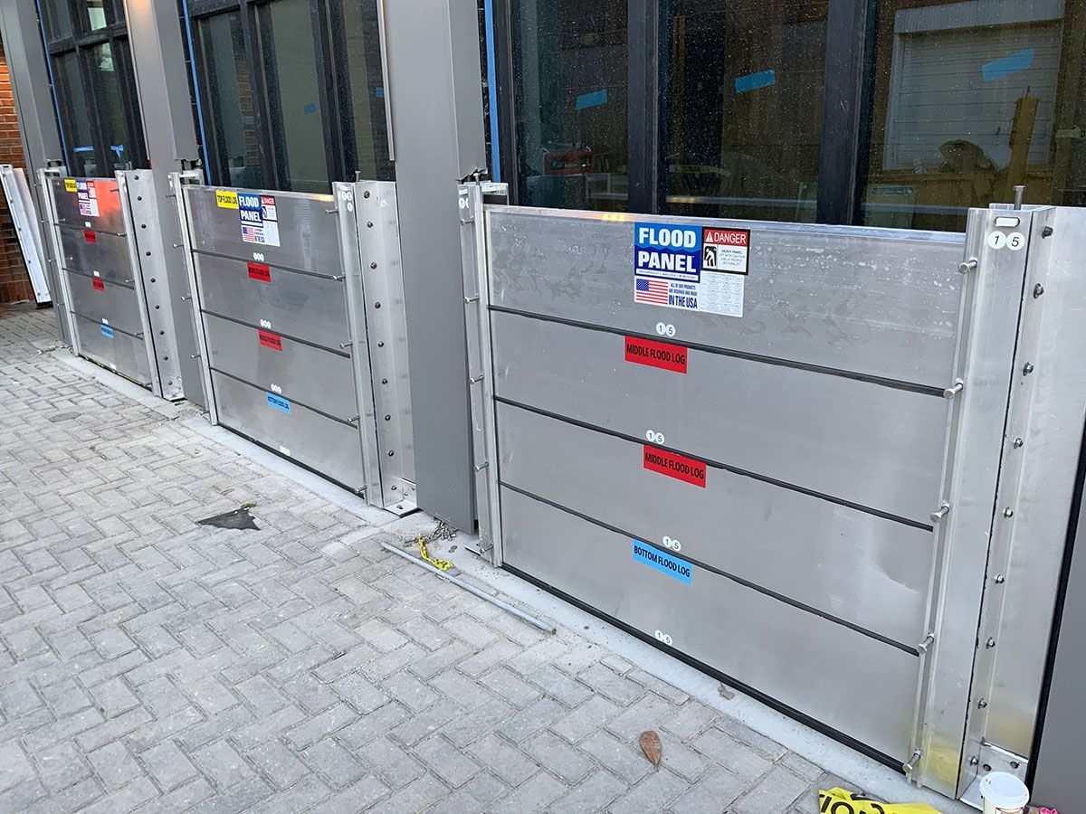 A row of stainless steel flood barriers on a sidewalk next to a building.