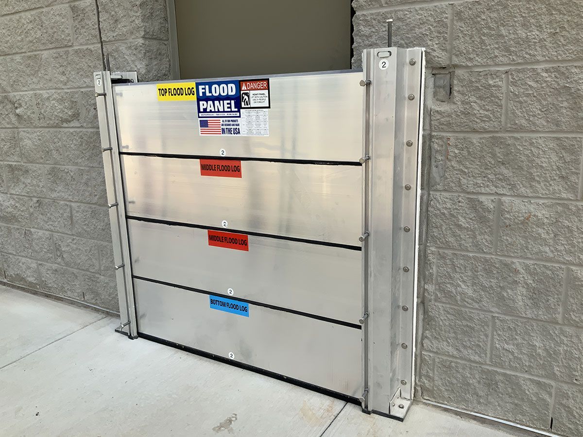 A flood barrier is sitting on the sidewalk next to a brick wall.