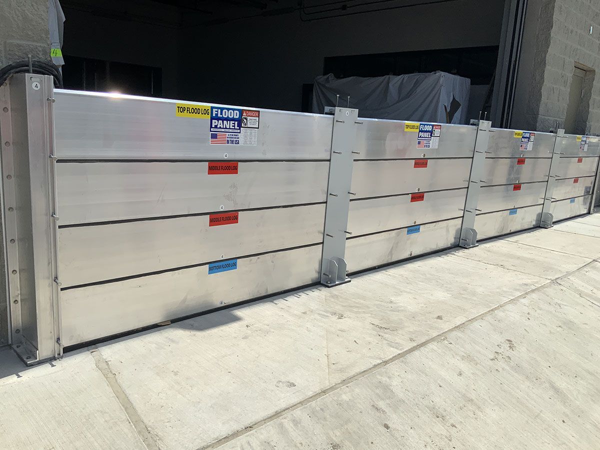 A row of aluminum flood barriers are lined up on the sidewalk in front of a building.