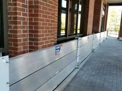 A brick building with a flood barrier on the sidewalk in front of it.