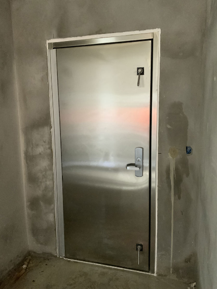 A stainless steel door is in a room with a concrete wall.