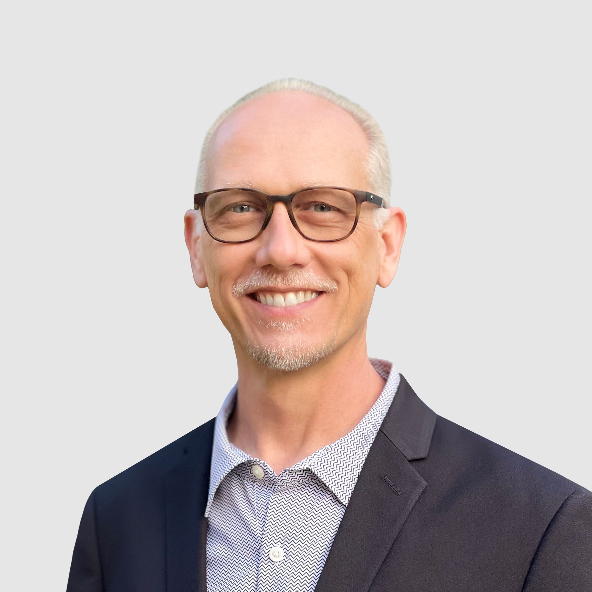 A man wearing glasses and a suit is smiling for the camera.