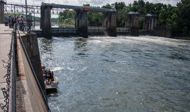 A boat is going down a river next to a dam.