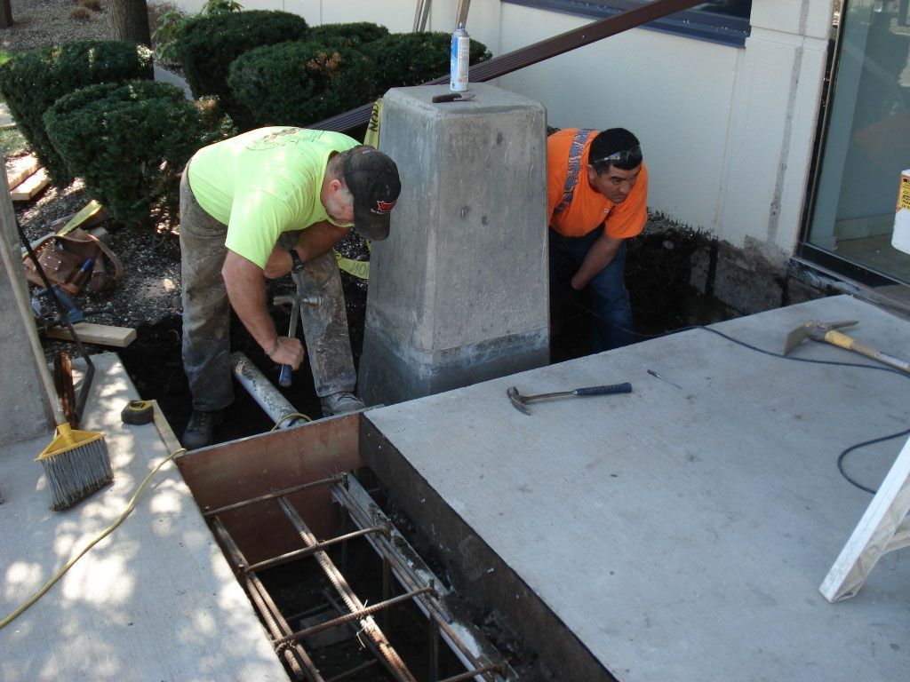 Two men are working on a concrete staircase in front of a building.