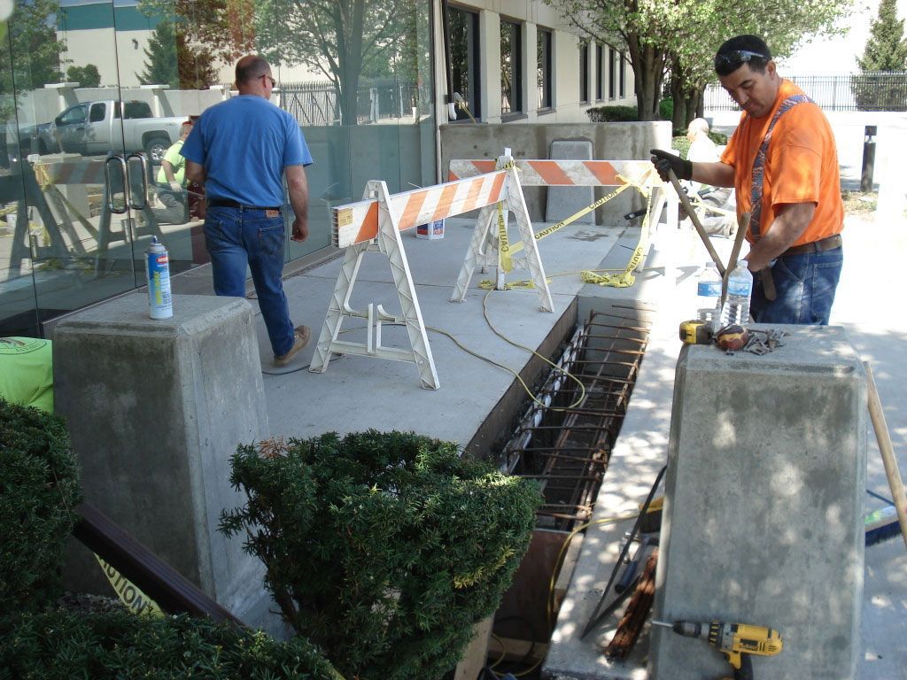 A man in an orange shirt is working on a sidewalk