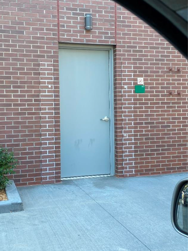 A brick building with a gray door and a green sign on it