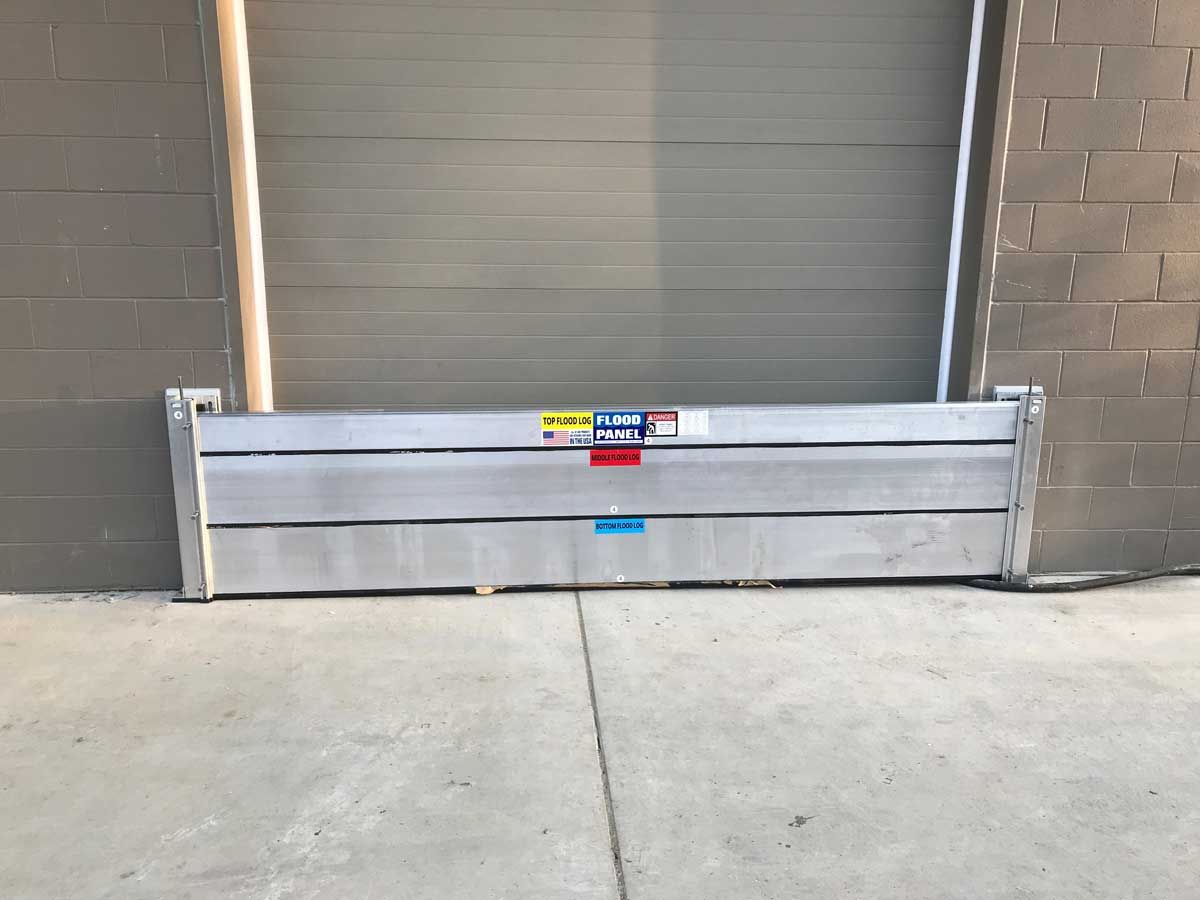 A flood barrier is sitting on the sidewalk in front of a garage door.