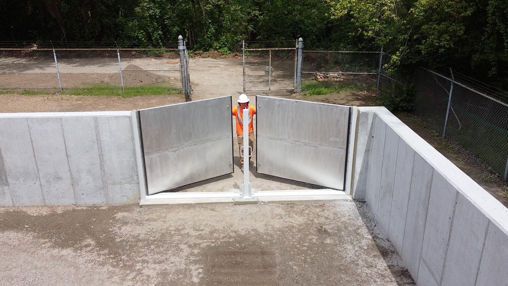 A man in an orange vest is standing in front of a metal gate.